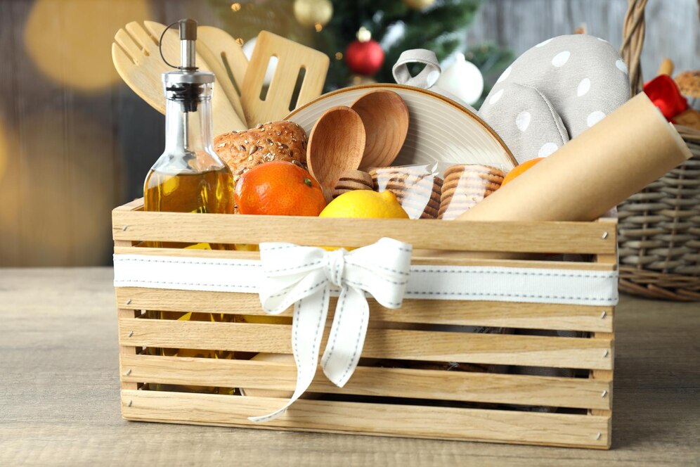 A wooden basket filled with kitchen items including a bottle of olive oil, fruits, wooden utensils, and a decorative ribbon.